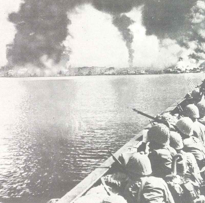 Japanese troops watch Manila burn from their landing craft.
